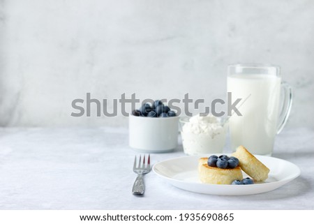 Cottage cheese pancakes with blueberry, sour cream and glass of milk on stone background.  Healthy Breakfast. 