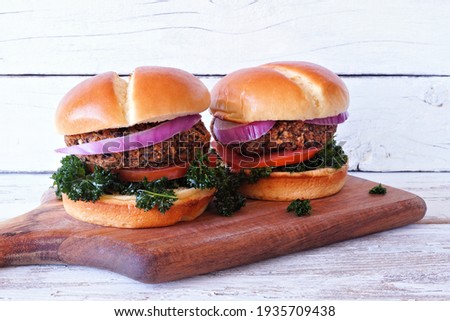 Vegan bean and sweet potato burgers with kale, onion and tomato against a white wood background