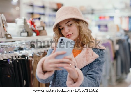 Pretty woman trying on a pink hat in the store making a selfie photo on the smartphone