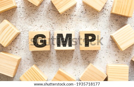 The word GMP consists of wooden cubes with letters, top view on a light background. Work space.
