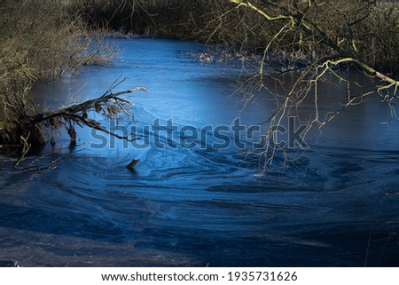 A beautiful picture of a small pond covered with ice. Blue icy water with trees in the background