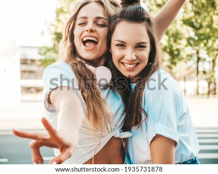 Portrait of two young beautiful smiling hipster female in trendy summer white t-shirt clothes.Sexy carefree women posing on street background. Positive models having fun, hugging and going crazy Royalty-Free Stock Photo #1935731878