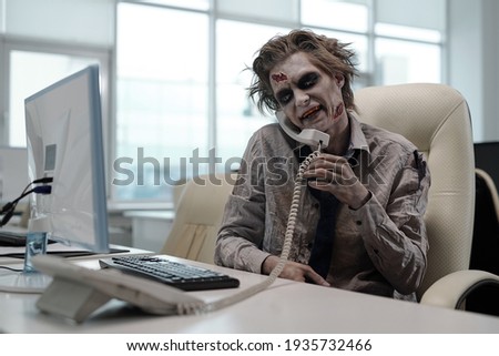 Zombie businessman with phone receiver between his shoulder and cheek looking at computer screen Royalty-Free Stock Photo #1935732466