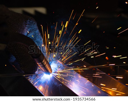 Metal welder works with a steel welder in a factory with protective equipment. Manufacture of metal structures and repair and construction services according to the concept of manual labor. Royalty-Free Stock Photo #1935734566