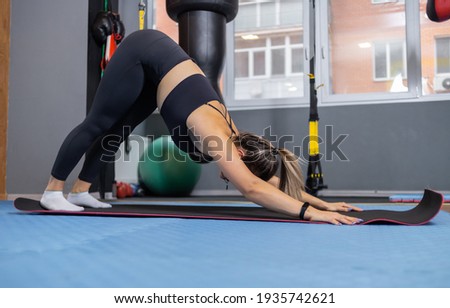 Sports young blonde woman in sportswear practicing yoga asana in room with sports equipment. Downward-facing dog pose. Healthy lifestyle