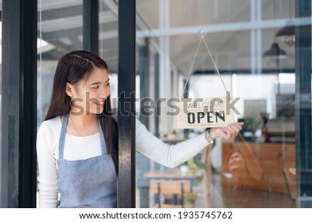Small business owner smiling while turning the sign for the reopening of the place after the quarantine due to covid-19. Close up of woman hands holding sign now we are open support local business. Royalty-Free Stock Photo #1935745762