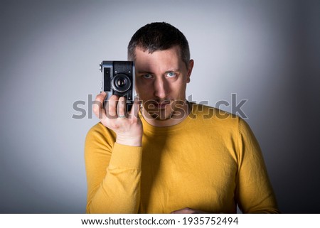 A man in a yellow sweater poses with a vintage film camera on a gray background. vignette effect on photo.