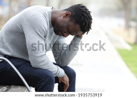 Profile of a sad black man complaining alone sitting on a bench in a park Royalty-Free Stock Photo #1935753919