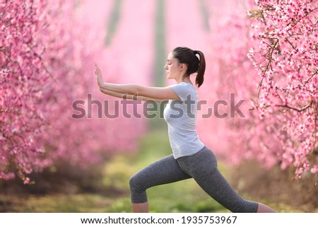 Side view portrait of a woman doing tai chi exercise in a pink flowered field Royalty-Free Stock Photo #1935753967