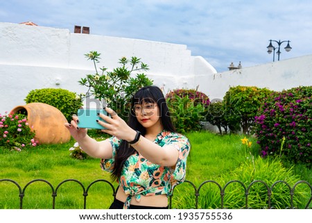 Young Asian tourist woman taking a selfie with a Canarian garden behind. He wears a floral shirt and glasses. Puerto de La Cruz is a tourist site in Tenerife.