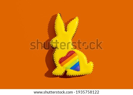 Lgbtqia pride. Gay solidarity. Bakery food decor. Conceptual art. Bunny gingerbread cookie with yellow icing rainbow heart ornament isolated on orange.