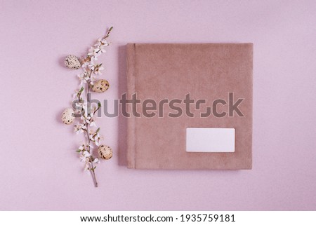 Flat lay with a pink photo album or book with a metal frame for the inscription, spring branches with flowers and Easter eggs on a pink background. Top view, copy space
