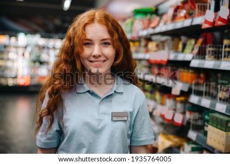 Portrait of a young woman working at supermarket during holidays. Woman doing a part time job grocery shop. Royalty-Free Stock Photo #1935764005