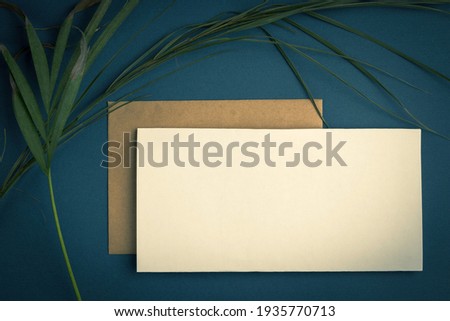 Blank white sheet mockup and vintage envelope on green background with palm leaves. Flat lay, top view.