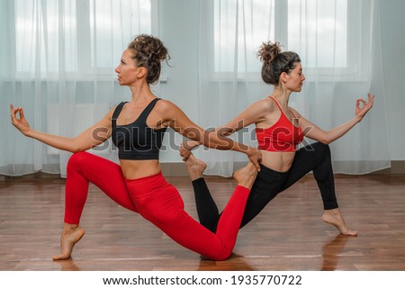 Two attractive athletic girls train asana yoga pose in red jumpsuits in the gym. A group of young women stretch out in the gym. Healthy lifestyle Concept