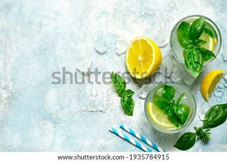 Cold summer lemonade with basil and lemon in a glass on a light blue slate, stone or concrete background. Top view with copy space. Royalty-Free Stock Photo #1935784915