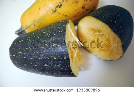 Double colour (green and yellow) the squashes or cucurbites lie on a white table top. One of them is cut in half.