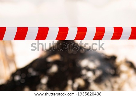 A terribly ominous picture of the end of a burning fire with a warning tape - fire extinguishing and protection means. Crime scene. Shallow depth of field
