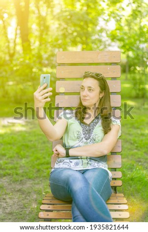 Young woman takes a selfie, sits on a bench in a city park. toned. vertical photo