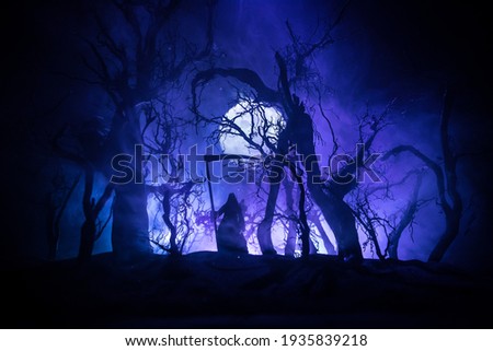 Death with a scythe in the dark misty forest. Woman horror ghost holding reaper in forest, halloween concept. Creative artwork table decorations in selective focus