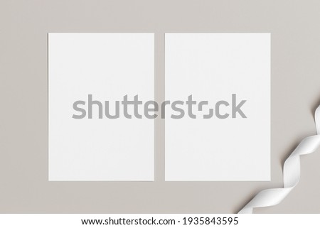 Two white invitation cards mockup with a satin tape decoration on a beige table. 5x7 ratio, similar to A6, A5. Royalty-Free Stock Photo #1935843595