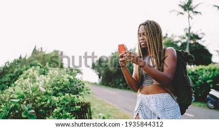 Millennial hipster girl with dreads reading received email checking content text during leisure time for adventures, dark skinned female tourist with rucksack using internet for networking during trip