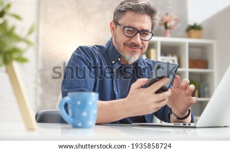 50s man checking news on phone at home. Confident happy smiling. Royalty-Free Stock Photo #1935858724