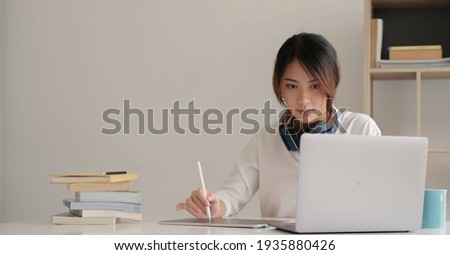 Young student watching lesson online and studying from home. Young woman taking notes while looking at computer screen following professor doing math on video call. Girl studying from home on pc.
