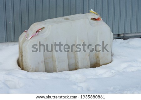 one gray plastic barrier stands in a snowdrift of white snow outside near the metal wall of the fence