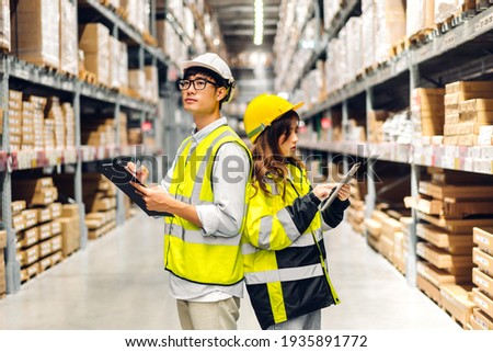 Asian two engineer in helmets team order details on tablet computer for checking goods and supplies on shelves with goods background in warehouse.logistic and business export