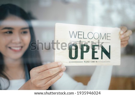 Small business owner smiling while turning the sign for the reopening of the place after the quarantine due to covid-19. Close up of woman hands holding sign now we are open support local business. Royalty-Free Stock Photo #1935946024