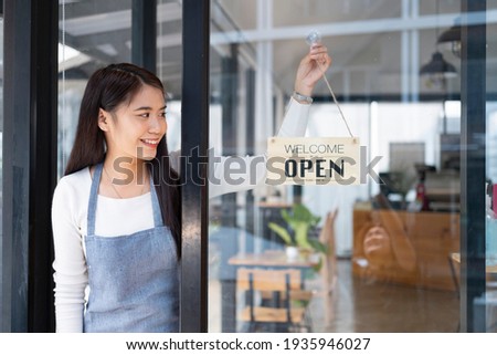 Small business owner smiling while turning the sign for the reopening of the place after the quarantine due to covid-19. Close up of woman hands holding sign now we are open support local business. Royalty-Free Stock Photo #1935946027