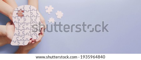 Adult and children hands holding brain with puzzle paper cutout, autism, memory loss, dementia, epilepsy and alzheimer awareness, world mental health day, world Parkinson day concept Royalty-Free Stock Photo #1935964840