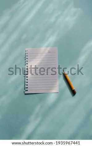 A blank sheet of paper and an old pencil on a light blue background with shadows. A page torn from a notebook. Top view at an angle.