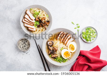 Chicken ramen, asian noodle soup. Two bowls of delicious homemade chicken ramen noodle soup with shiitake mushrooms on a grey concrete background, table top view Royalty-Free Stock Photo #1936005136