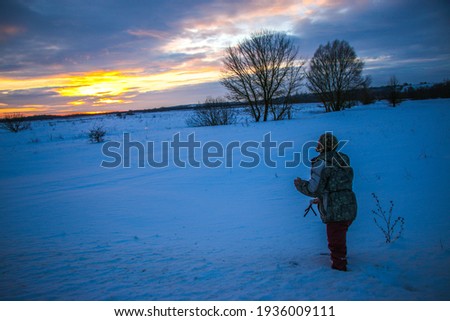 Man with phone on tripod making time-lapse photographs of winter zidio sunset.