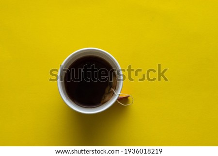 A disposable white cup full of tea, yellow background