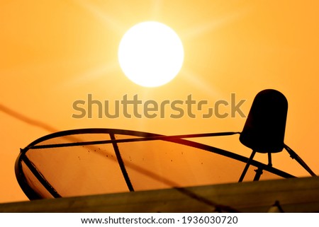 Satellite technology dish receiver on sunrise and golden sky background, blurred roof forground on light ray of sunny, antenna on roof for sent and receive data information network on home of tv