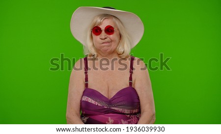 Portrait of old granny traveler model on summer vacations. Funny silly senior pensioner woman tourist in swimsuit, fooling around making stupid face brainless dumb expressions on chroma key background