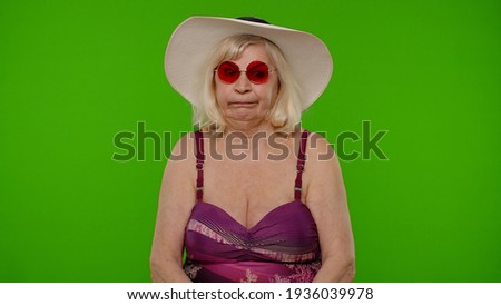 Funny silly senior pensioner woman tourist in swimsuit, fooling around making stupid face brainless dumb expressions on chroma key background. Portrait of old granny traveler model on summer vacations
