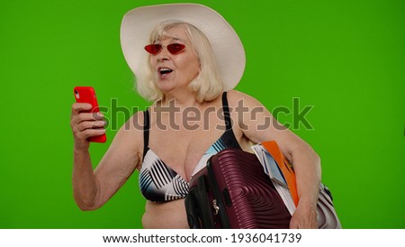 Mature woman traveler blogger in sunglasses, taking selfie portrait photo, video call on smartphone. Senior grandmother in swimsuit bra on chroma key. Tourism, summer holiday vacation, trip to sea