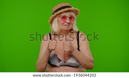 Elderly woman tourist in swimsuit and sunglasses, looking at camera, smiling, showing thumbs up on chroma key. Summer traveling abroad on holidays weekends. Retired grandmother on journey to seaside