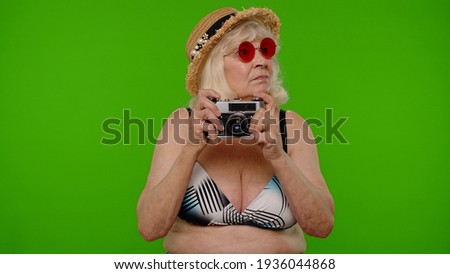 Travel, long awaited summer holiday vacation, beach party. Grandmother relaxing on sea resort. Senior woman tourist photographer in swimsuit taking photos on old retro camera, smiling on chroma key