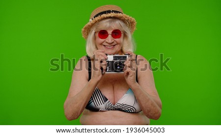 Travel, long awaited summer holiday vacation, beach party. Senior woman tourist photographer in swimsuit taking photos on old retro camera, smiling on chroma key. Grandmother relaxing on sea resort