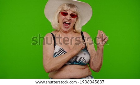 Senior pensioner woman tourist in swimsuit bra, red sunglasses and hat dancing, celebrating, smiling, posing on chroma key background. Portrait of exited old granny traveler model on summer vacations