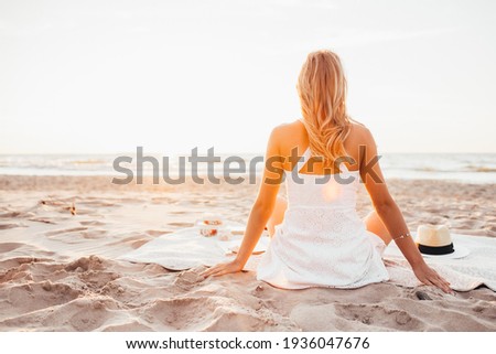 Back view of young slim woman walk alone on the beach or ocean and look at the horizont. Female wear white summer dress.