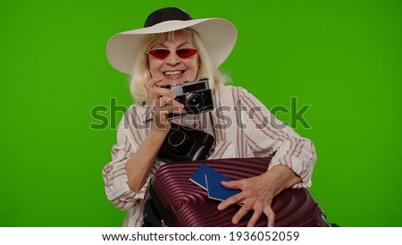 Mature woman photographer traveler in red sunglasses taking picture photos on retro camera. Senior grandmother with passports on chroma key background. Tourism, summer holiday vacation, trip to sea
