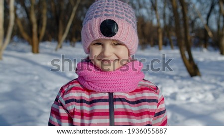 Smiling shy child kid looking at camera, fooling around, making faces. Portrait of cute girl in winter snowy park forest in frosty day. Children having fun at Christmas holidays time