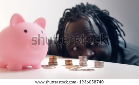 Financial decision, investments and savings. Funny man looking into the coins in front of the piggy bank. Racking focus. High quality photo