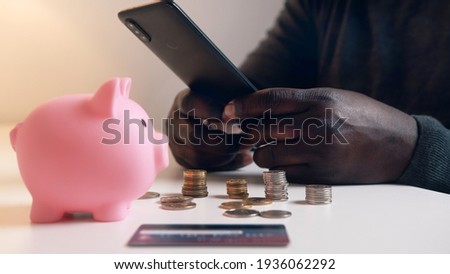 Man using phone to check his bank account. Piggy bank credit card and coins on the table. Investment using mobile app. High quality photo